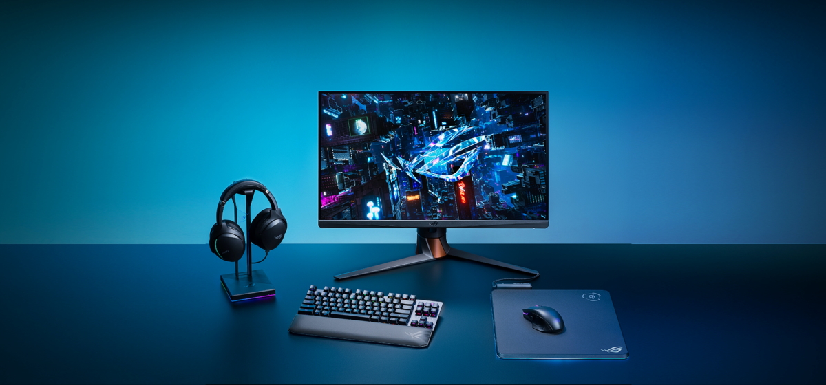 The ROG Strix Scope RX TKL Wireless Deluxe in wireless 2.4 GHz mode in a desktop setting, complete with a display, mouse and mousepad, and a pair of headsets