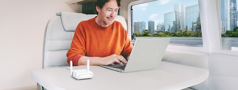A man in an RV using a laptop, with the ASUS RT-BE58 Go placed on the table.