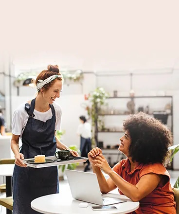 A guest using café WiFi while working on a laptop, with a friendly server smiling and serving food.